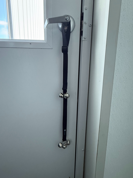 Dog training Potty Bells displayed on a silver door handle on a white door.